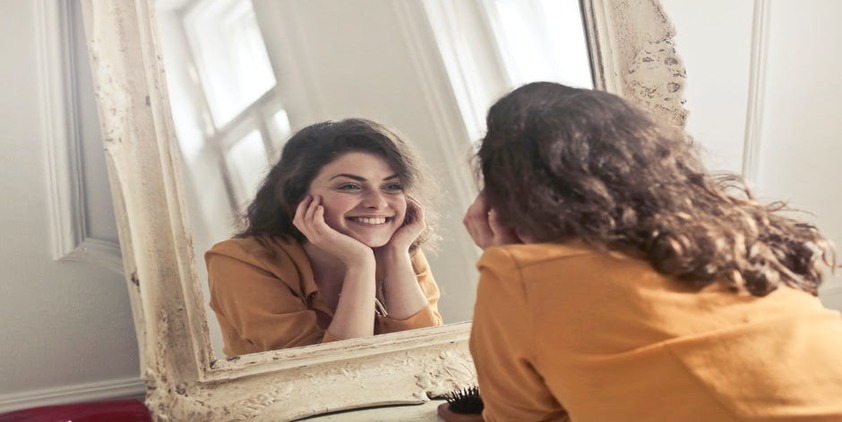 Pexels. Woman in yellow blazer looking in the mirror and smiling