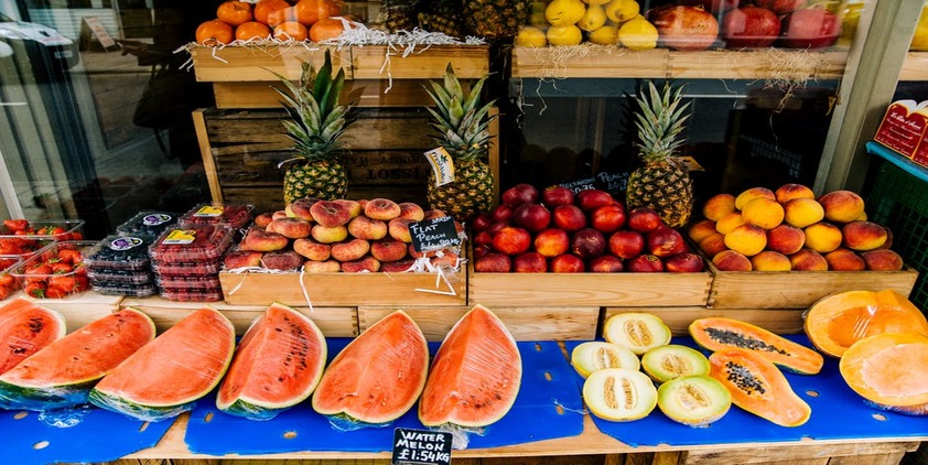Pexels. Fruit stand including peaches, watermelon, pineapple, strawberries, and apples