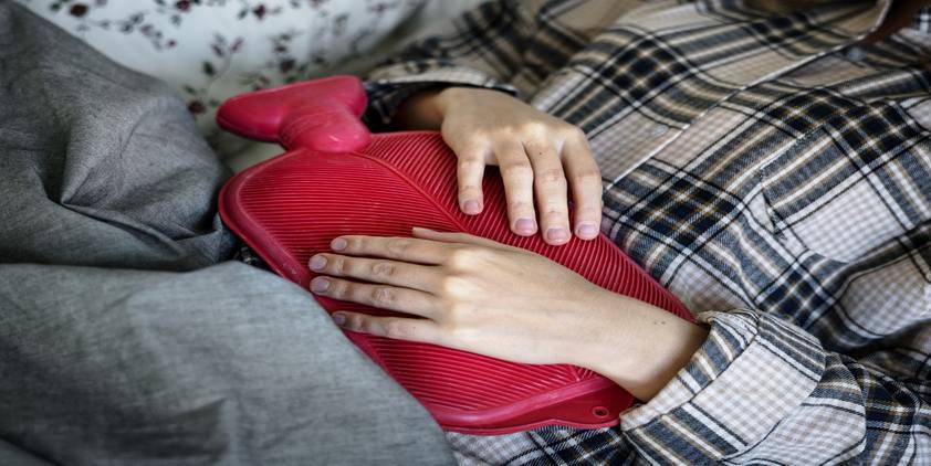 unsplash. woman in pajamas on couch holding red hot water bottle
