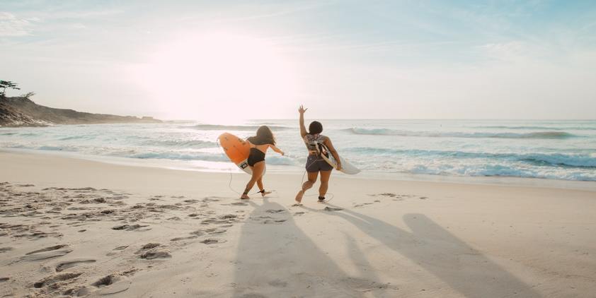 unsplash. two women on the beach with surfboards