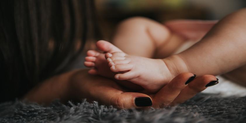 Unsplash. Woman with black nails holding baby's feet