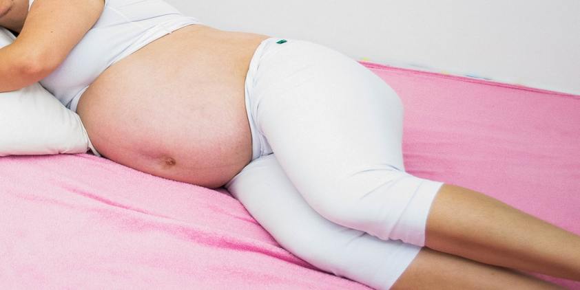 Unsplash. Pregnant woman laying on pink towel in sports bra and pants