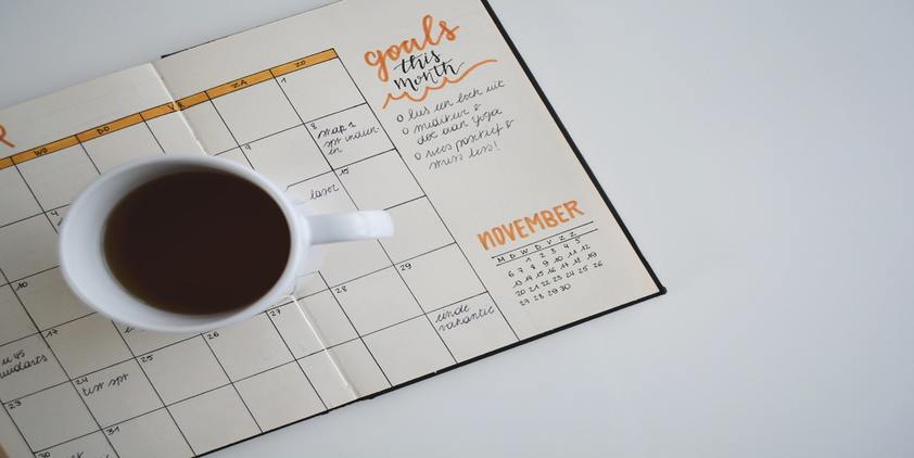 Unsplash. Handwritten calendar on notebook with orange highlights. Coffee cup in the middle.