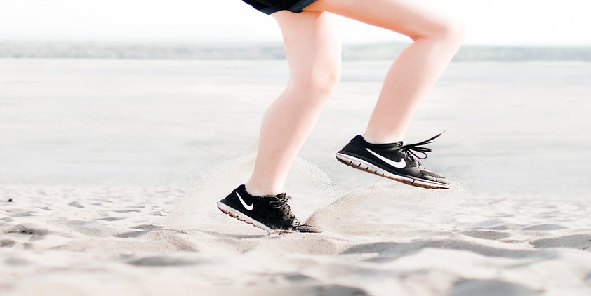 Unsplash. Woman running on beach in black sneakers