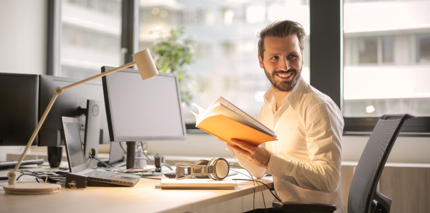 A man sits at his desk in his office and smiles while he works