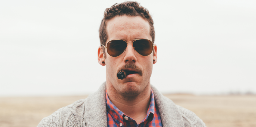 A man with a big mustache and sunglasses smoking a cigar