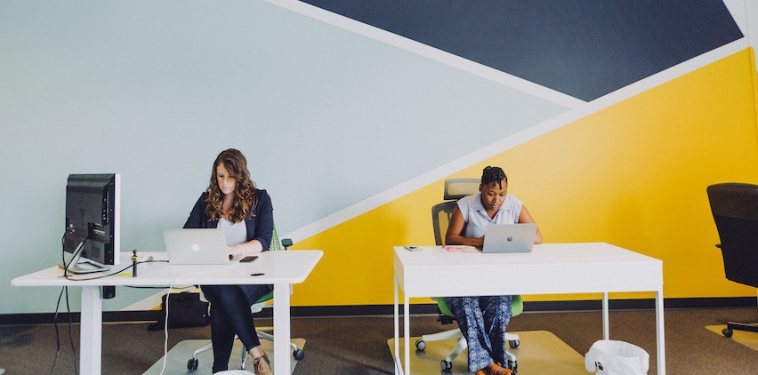 Two women sit at desks in their office.