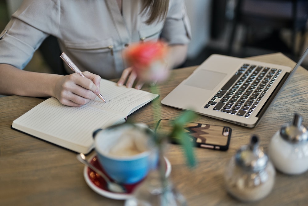 A woman writing in a notebook with a laptop