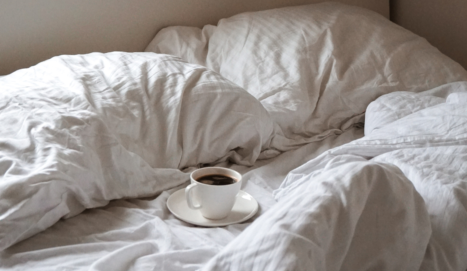 A bed with a cup of coffee on the sheets