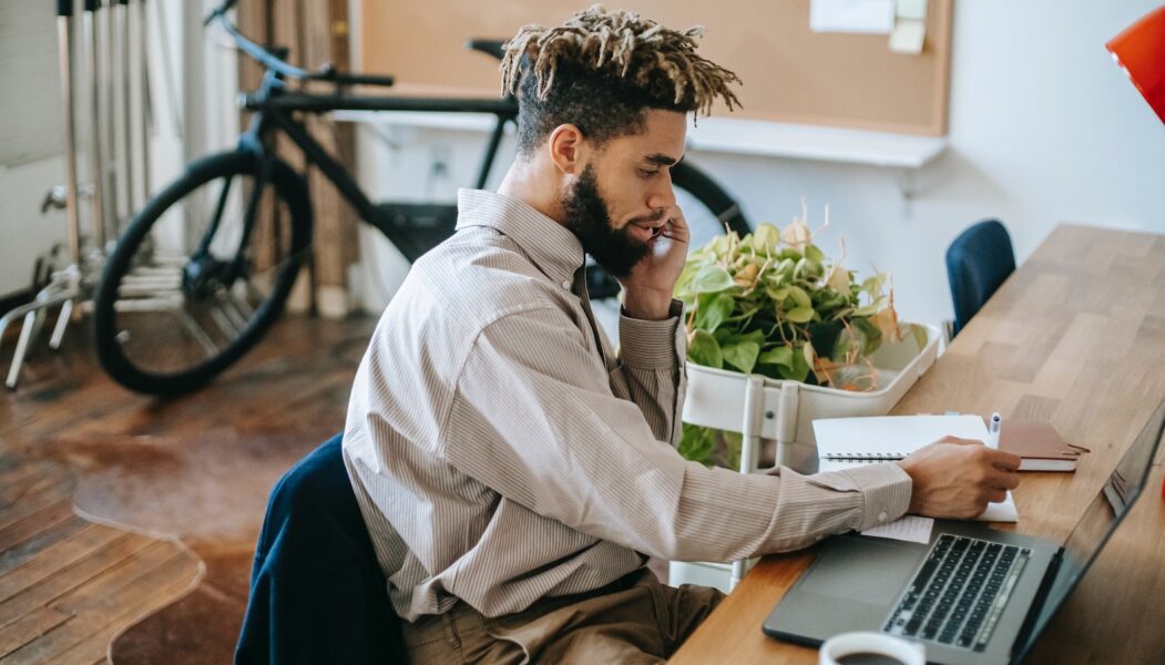 A man working on a laptop while talking on the phone.