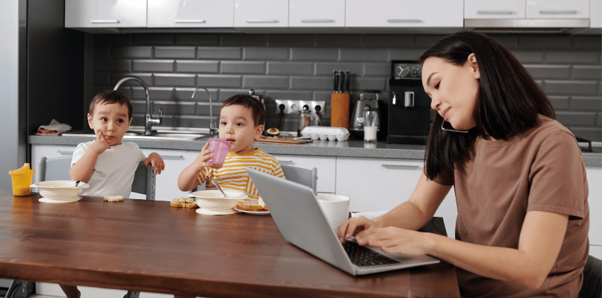 woman freelancing on phone and laptop in kitchen with children and working from home